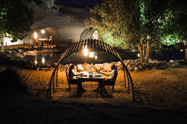 Dine under the stars in a serene desert oasis surrounded by softly glowing lights as you savor exquisite cuisine and unwind amidst the enchanting beauty of the Dubai dunes.